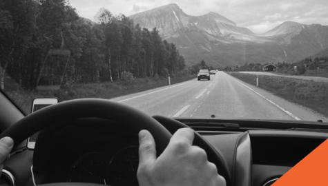 hands on the wheel of a car driving down the highway towards mountains